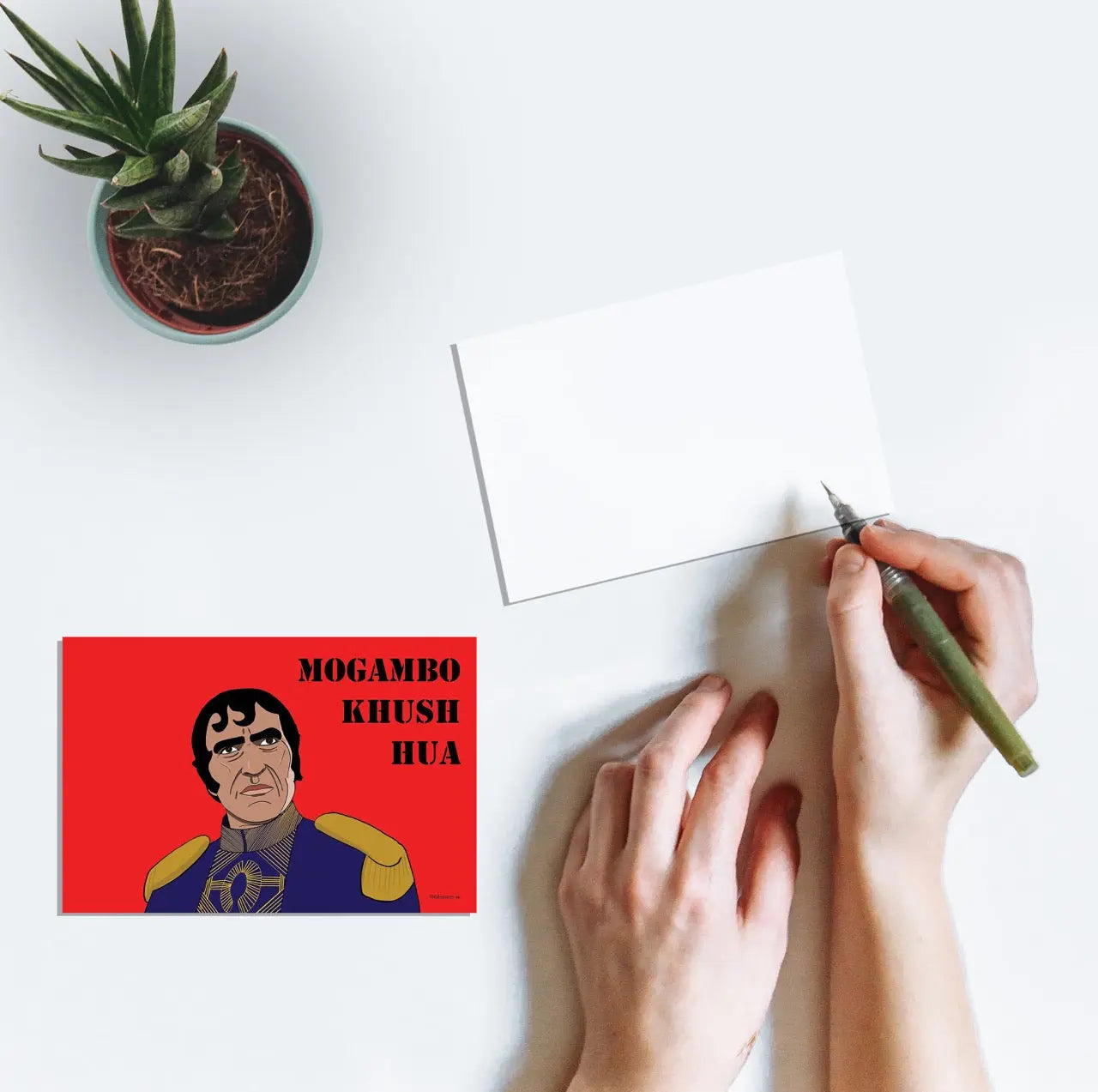 A person writing on a postcard with artwork of the character Mogambo played by Amrish Puri from the Bollywood film Mr. India with the text "Mogambo Khush Hua"