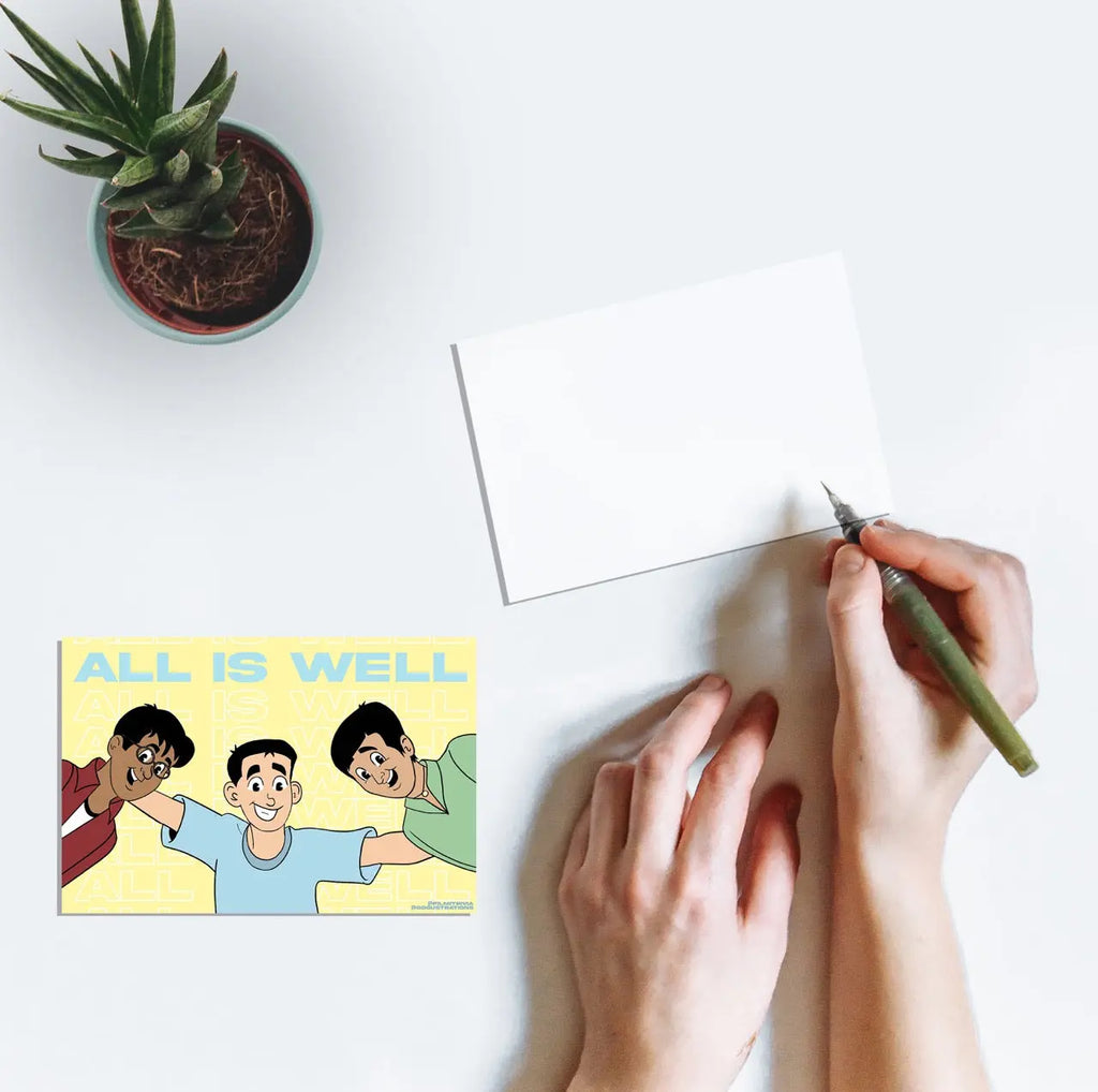 A person writing on a postcard featuring line art from the Bollywood film 3 Idiots (2009) featuring Rancho (Aamir Khan), Raju (Sharman Joshi), and R. Madhavan (Farhan Qureshi) with the text "All is Well".