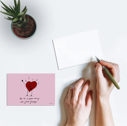 A person writing on a postcard with artwork of a heart singing and the text "Har dil jo pyaar karega woh gaana gayega" from the Bollywood film Har Dil Jo Pyar Karega (2000).