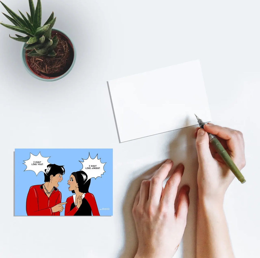 A person writing on a postcard with line art of Shah Rukh Khan and Kajol saying the dialogues "I don't like jokes" and "I don't like you" from the Bollywood film Kuch Kuch Hota Hai.