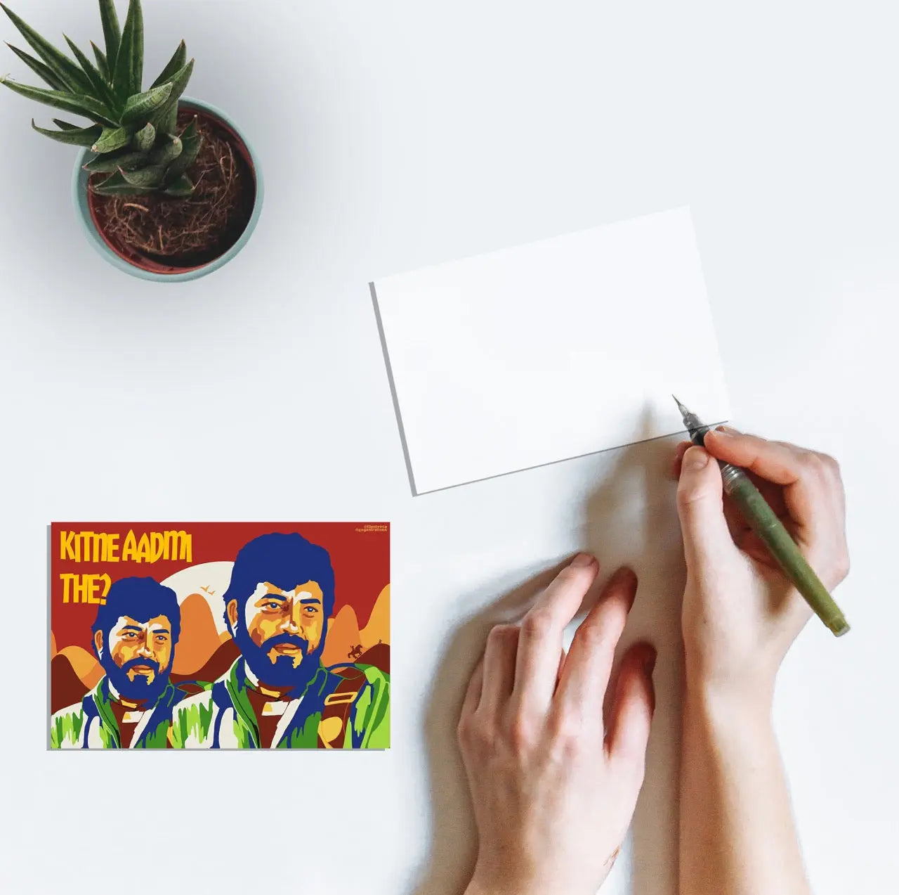 A person writing a postcard with artwork featuring Gabbar Singh from the Bollywood movie Sholay (1975) and the text "Kitne Aadmi The?".