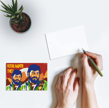 A person writing a postcard with artwork featuring Gabbar Singh from the Bollywood movie Sholay (1975) and the text "Kitne Aadmi The?".